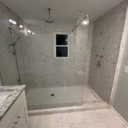 Modern bathroom with a walk-in shower, marble tiles, a glass partition, and a window on the shower wall.