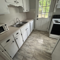 Small kitchen with white cabinets, stainless sink, microwave, stove, and a door leading outside; gray tiled floor.