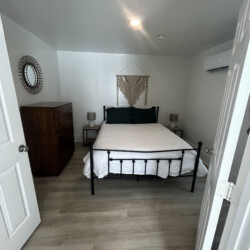 Small bedroom with a double bed, two nightstands, dresser, wall art, and an air conditioner on the right wall.