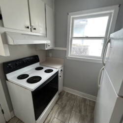Small kitchen with electric stove, refrigerator, white cabinets, tile floor, and a window letting in natural light.