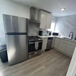Modern kitchen with stainless steel appliances, white cabinets, marble backsplash, and light wood flooring.