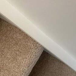 Close-up of a carpeted staircase with a white wall above, viewed from an angle.