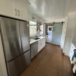 Narrow kitchen with stainless steel appliances, white cabinets, wood floor, and a blue sliding barn door at the end.