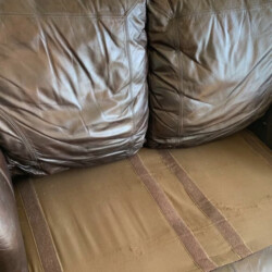 Screenshot Brown leather couch with missing seat cushions, exposing the underlying fabric and Velcro strips.